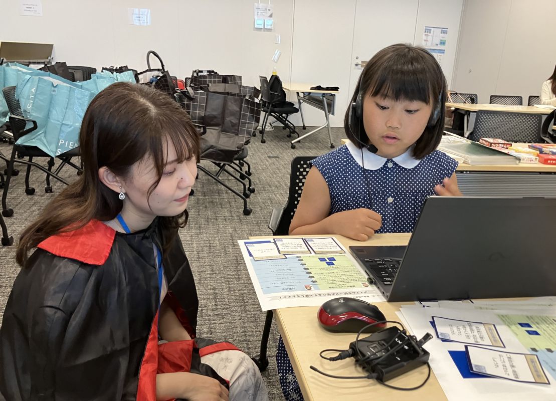 ヘッドセットをつけた小学生が社員に見守られながら損害サービス案内のロールプレイングを行っています